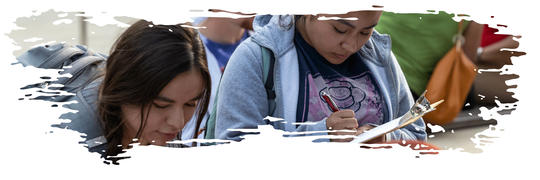 Students filling out a form on a clipboard to receive information on a student organization.