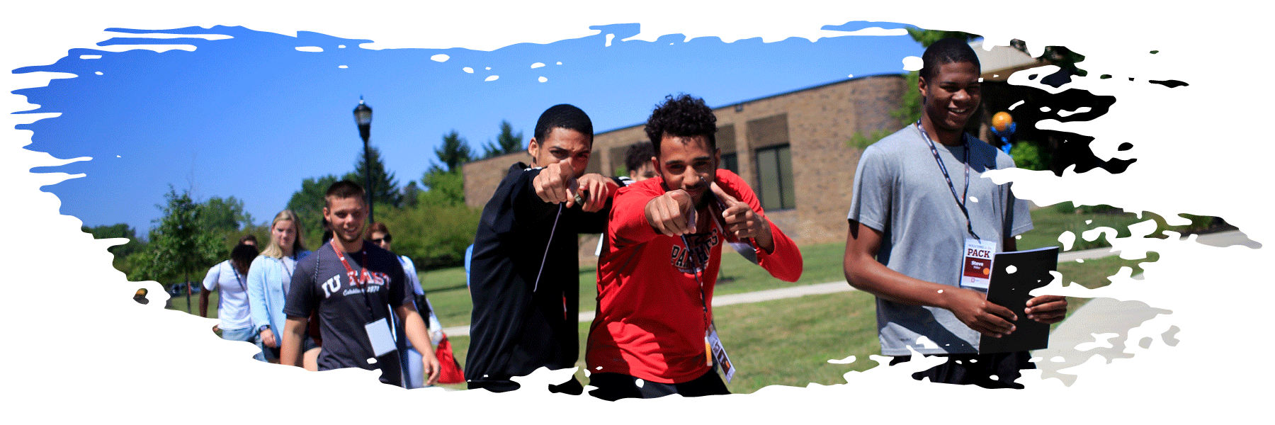 Two students walking on campus in a group stop to point at the camera in an excited and inviting manner