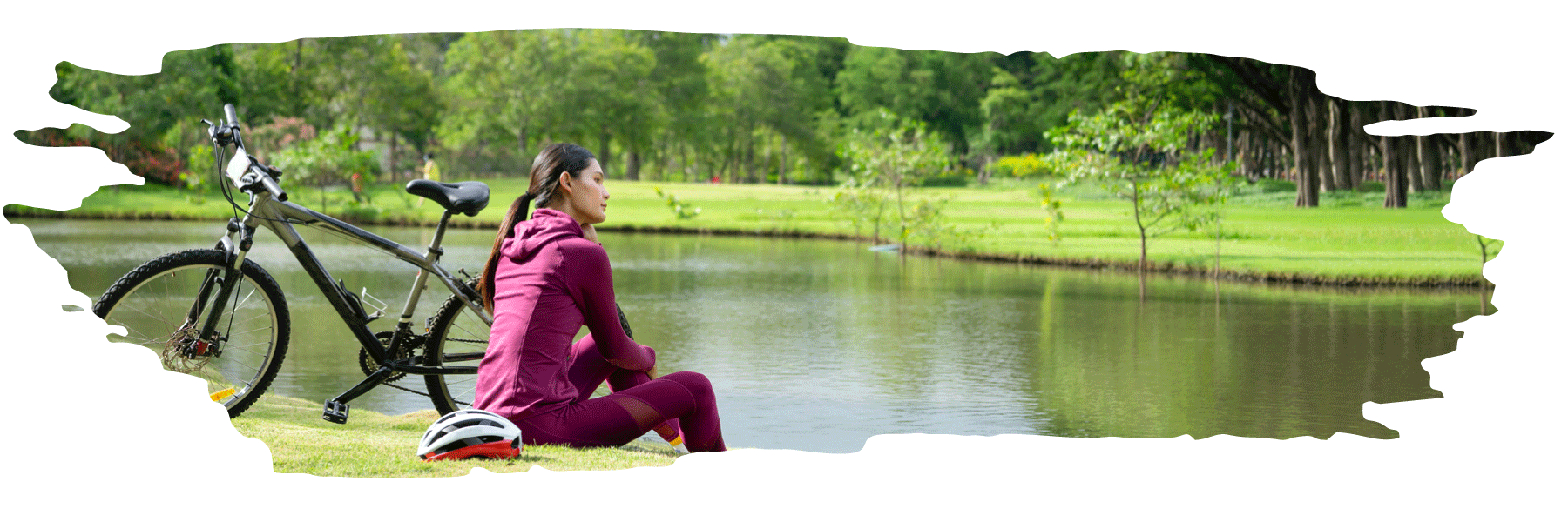 A female sitting at the edg of a small lake next to a bicycle and helmet