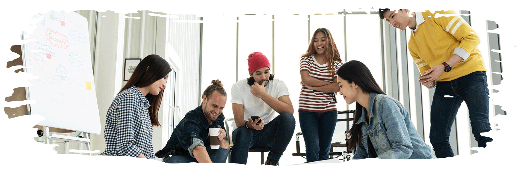 Six smiling or laughing students are looking at the same, central item on the floor