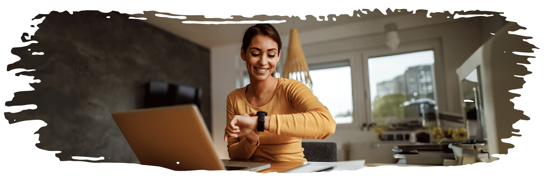 A young woman, sitting at her computer, is looking at her wristwatch