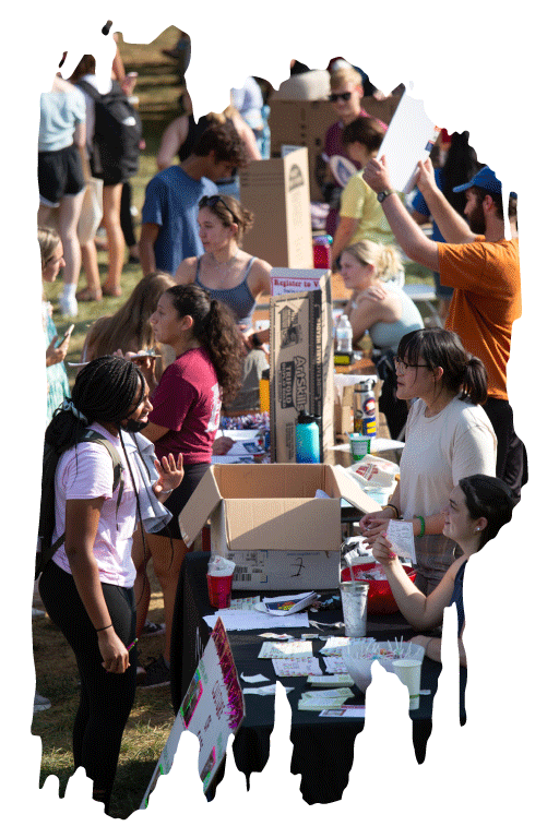 A new student is talking to an officer of a student organization in a crowd of students and information tables at an involvement fair.